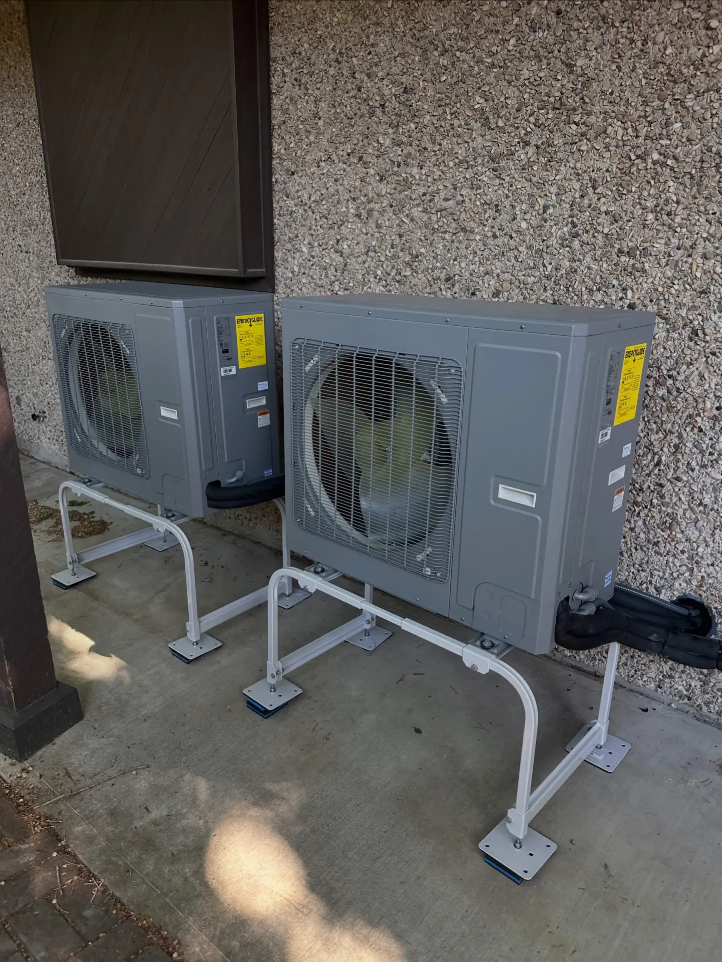 Two outdoor heat pump units on raised stands beside a home