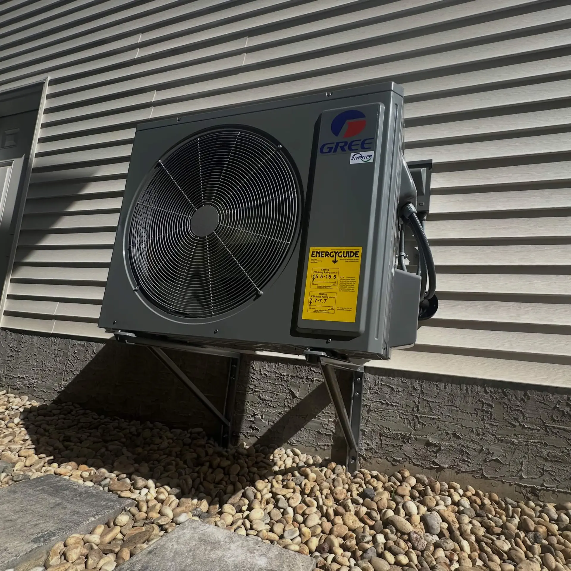 Gree inverter heat pump mounted on wall brackets above landscaping rock